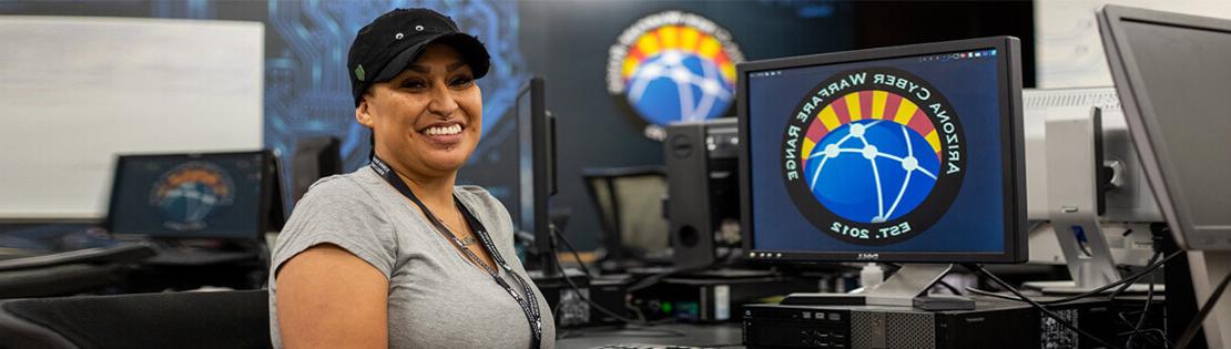 A student sits smiling at a computer in Pima's Cyber Warfare Range class