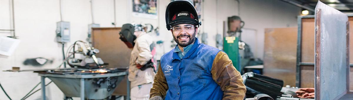 A student pauses and poses for a photo while working on welding project