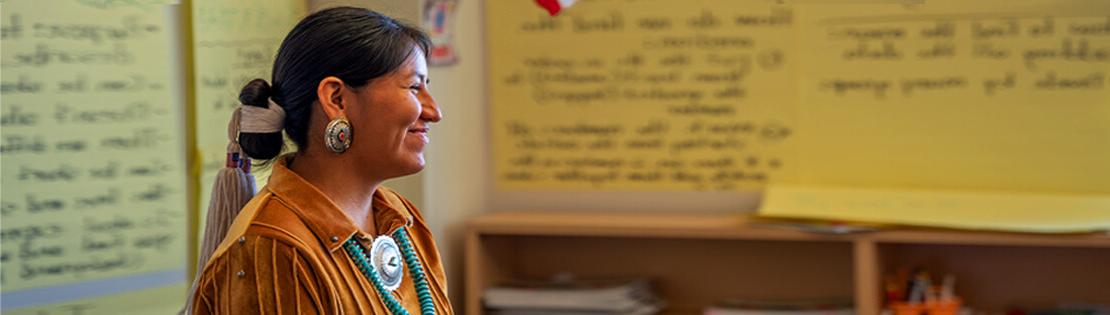 A Native American woman stands smiling in a Pima classroom