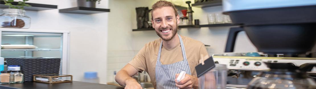 A Small business owner stands smiling behind his coffee counter